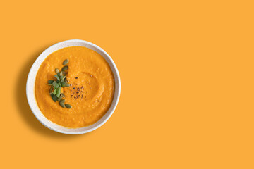 Pumpkin soup decorated microgreens amd pumpkin seeds isolated on orange background. View from...