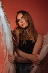 A beautiful girl is standing in jeans with big white wings. On a red background