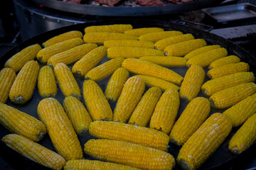 Healthy street food to go: Lots of yellow corn cobs cooked in a large cauldron over an open fire. Delicious food cooked over an open fire is offered at the street food fair, event, festival.