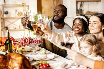 Happy family celebrate Thanksgiving day, sitting at table with roasted turkey and holiday traditional food, dishes. Drinking wine