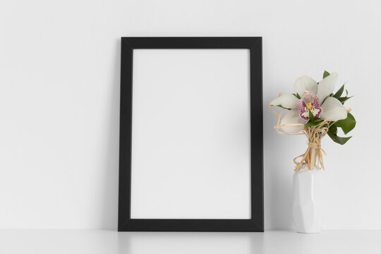 Black frame mockup with a orchid on the white table.