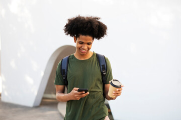 Handsome African man drinking coffee outdoors. Urban guy using the phone.