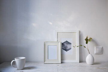 Scandinavian style. Interior Design. A white cup, a small vase with a dried eucalyptus branch, a two photo frames are on the table. Empty space for text