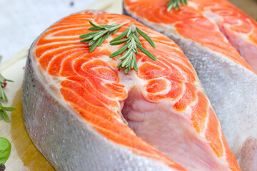 Raw red salmon fish slices with rosemary in the kitchen on light wooden background.