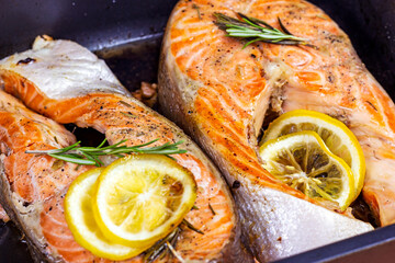 Fresh roasted red salmon fish steaks with herbs, spices and lemon on black metal plate background.