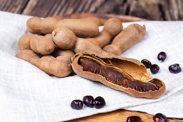 Fresh brown tamarind fruit pods ripe with seeds on light textile background close up.