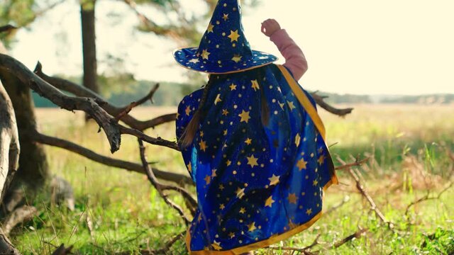A small child dressed in a wizard costume is playing in park, Halloween. A child plays in mantle of magician at sunset, fantasizes. Happy childhood, family. Kid dreams, fantasies to become wizard