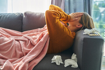 Tired ill woman lying on sofa and covering her eyes