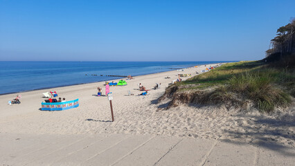 Norddeutscher weißer Sandstrand an der Nordsee. Vereinzelte Touristen sonnen sich. Blaues ruhiges Meer vor blauem Himmel und grasigen Dünen. Nordseestrand in Deutschland.