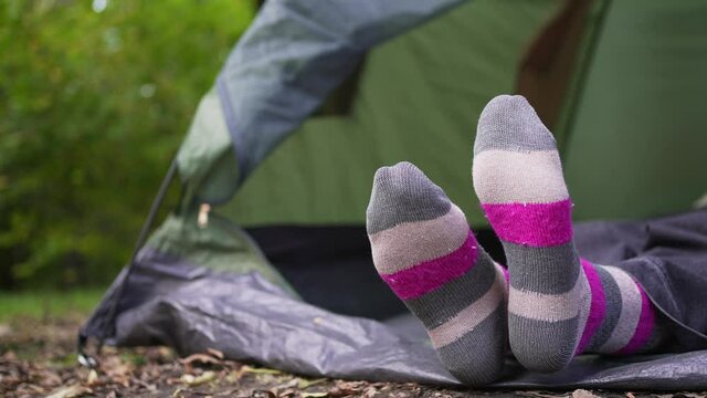 A woman in bright multi-colored socks lies in a tent in the woods. Campground. Relaxing in the wild alone