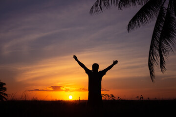 Silhouette of an adult man with arms outstretched in an attitude of happiness. Happy man at sunset.