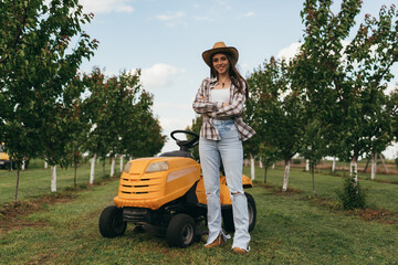 woman posing beside lawn mower in orchard