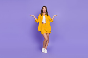 Full body photo of funny millennial brunette lady hold empty space wear yellow suit isolated on violet background