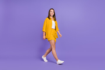 Full length profile photo of sweet millennial brunette lady go wear yellow outfit sneakers isolated on purple background