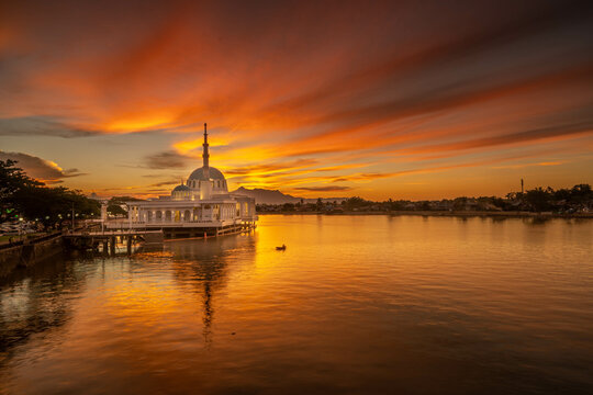 the view of a mosque during the azan solat magrib on the banks of the sarawak river which is the color of the red sunset