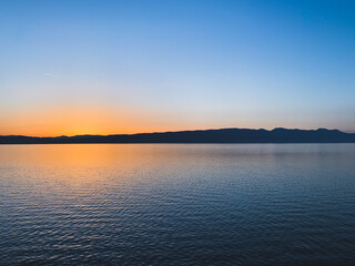 Fototapeta na wymiar Idyllic orange sunset at the lake, silhouette of the mountains background