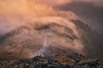 Mist and fog over the top of the hill in mountains evening orange light. autumn mood in hills