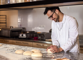 Young male baker preparing dough for bread in modern manufacturing.