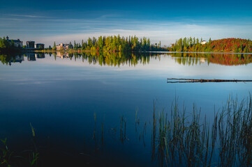 Obraz premium Beautiful foggy morning. Lake coast trees symmetrically reflect in the river water. Fog over autumn lake water.