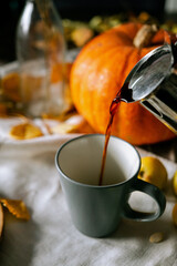 There is a layout of pumpkin and autumn leaves on the kitchen table with cappuccino 