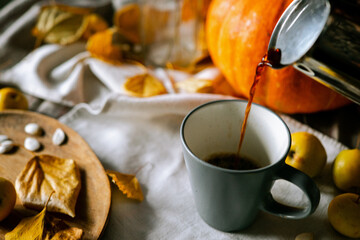 There is a layout of pumpkin and autumn leaves on the kitchen table with cappuccino 