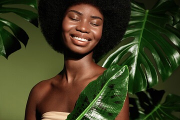 Organic cosmetics concept.  Beauty portrait of young beautiful african american woman with posing with banana leaf curly hair against green exotixc plants background.
