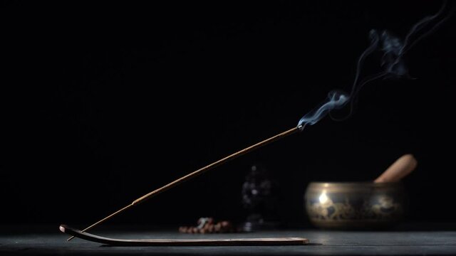 Asian incense stick in stick holder burning with smoke on black background, close up, copy space. Meditation, yoga, self development and sound therapy concept