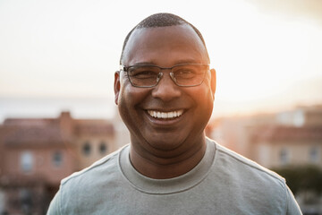 Happy senior african man looking at camera outdoors at sunset - Focus on face - obrazy, fototapety, plakaty