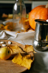 There is a layout of pumpkin and autumn leaves on the kitchen table with cappuccino 