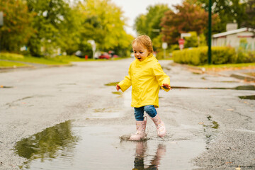 Funny cute baby girl wearing yellow waterproof coat and boots playing in the rain