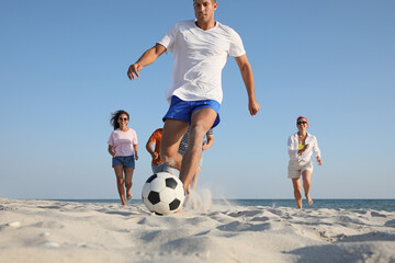 Group of friends playing football at beach, focus on ball