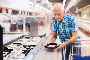 elderly retired senor buying sushi in buffet department of supermarket
