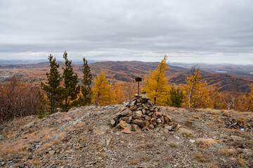 On the mountain lies a bunch of stones collected in a hill with a sign. Mountain landscape with panoramic views of the surroundings, obese clouds fly low over the horizon, dull autumn time.