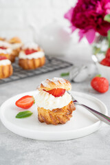 Delicious homemade small cakes profiterole choux pastry with custard, strawberry and icing powder on a gray concrete background. Copy space.