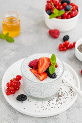 Vanilla chia pudding with fresh berries and honey in a glass on a gray concrete background. Superfoods concept. Copy space.