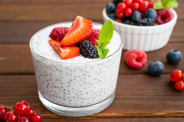 Vanilla chia pudding with fresh berries and honey in a glass on a dark wooden background. Superfoods concept. Copy space.