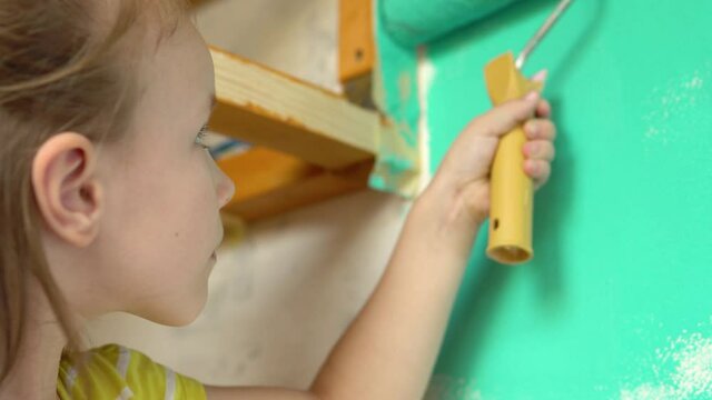 Little beautiful girl paints the wall with a roller green. She smears the paint on the wall.4k
