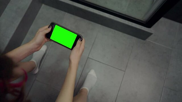Young woman sitting on a toilet watching media on her mobile