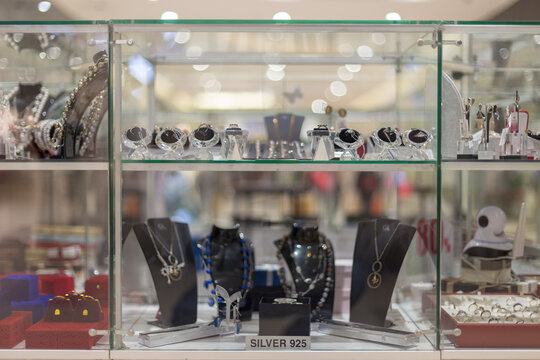 A variety of beautiful silver jewelry on a white showcase under glass in a jewelry store.