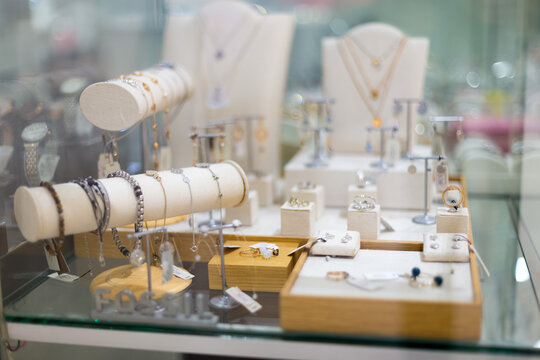 A variety of beautiful silver jewelry on a white showcase under glass in a jewelry store.