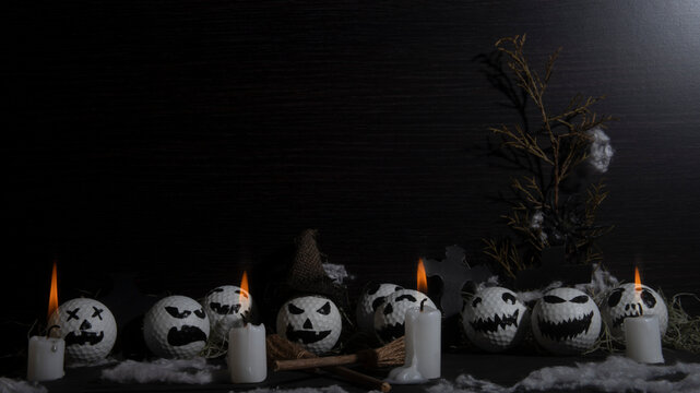 HALLOWEEN, GOLF BALLS DECORATED LIKE PUMPKINS WITH TERRORIFIC FACES WITH CANDLES, FOLIAGE, CROSSES, INSECTS ON RUSTIC WOODEN TABLE AND DARK BACKGROUND WITH SPACE FOR TEXT