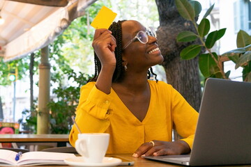 Cheerful black woman with credit card using laptop