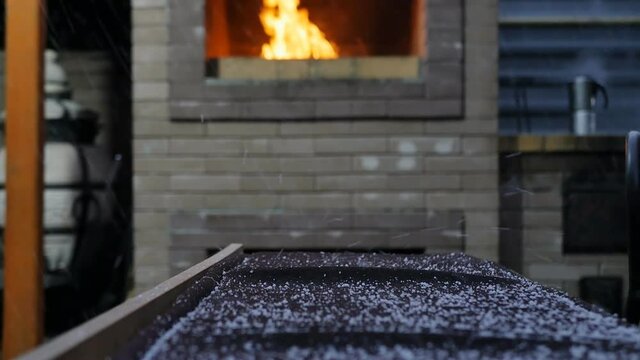 slow motion, DOF: A fire is burning in an outdoor fireplace, snow is falling and coffee is being brewed on a brick stove.