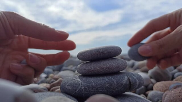 Female hands builds stone stacks pyramid on pebble beach. Hands putting stones on the pile of flat stones.