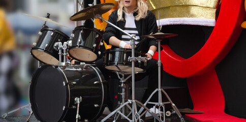 Rapaz a tocar bateria ao num palco ao ar livre - cabelo comprido e roupa preta