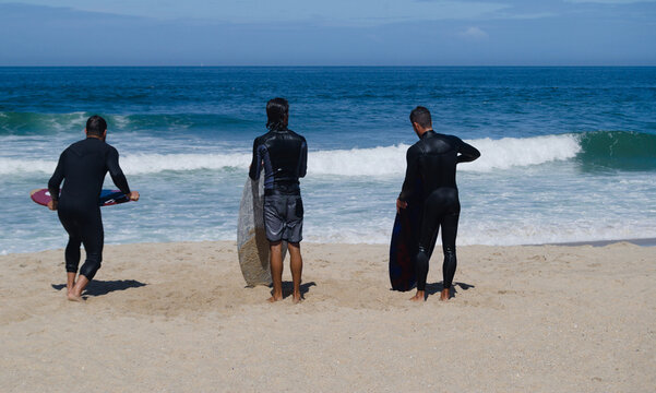Bodyboard, desporto radical, tr&ecirc;s homens na praia a praticar bodyboard, dois esperam o melhor momento para ir &aacute; &aacute;gua um a correr com a prancha na m&atilde;o para apanhar uma onda