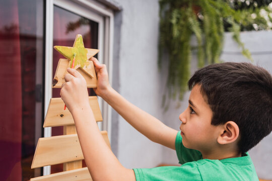 Boy painting star of wooden Christmas tree