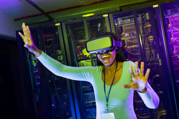 Happy african american female computer technician wearing vr headset and working in server room