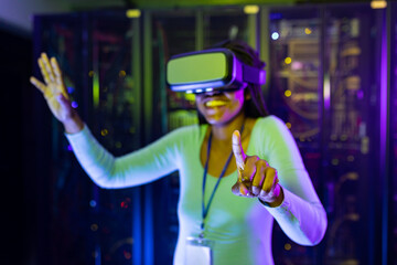 Happy african american female computer technician wearing vr headset and working in server room