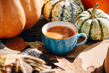 autumn still life with a cup of coffee. autumn leaves, pumpkins, a plaid and a hat on a wooden table and a cup of hot aromatic coffee in the center.